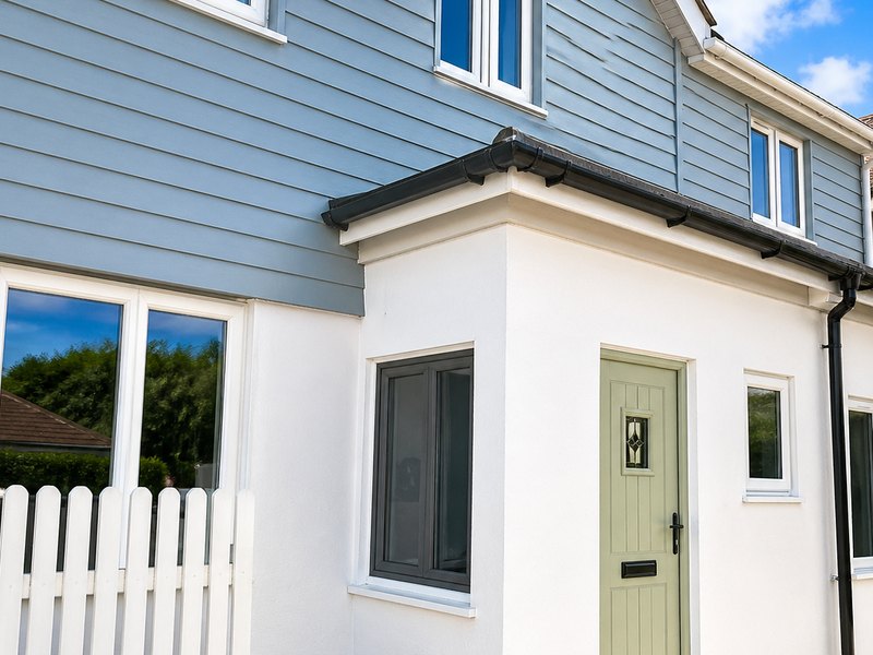 A white silicone rendered elevation with a green front door, beneath light blue cladding
