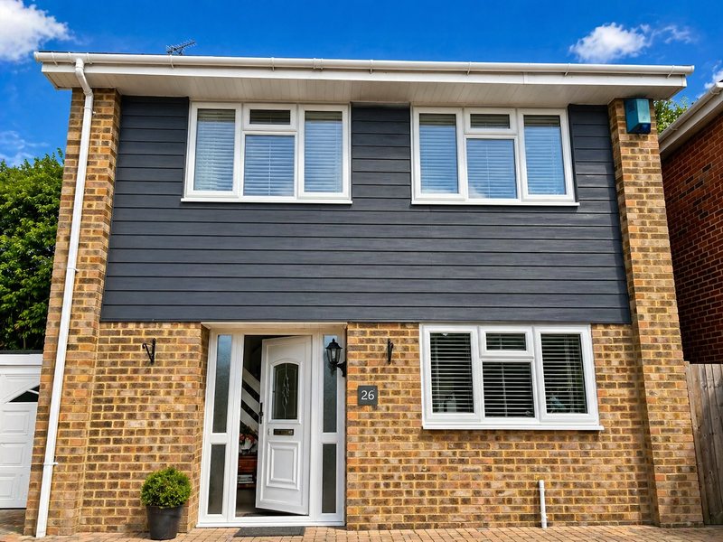 Dark grey cladding to the first floor of a detached house, with brick piers below