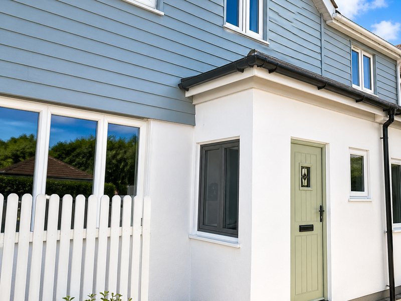 Light blue cladding meeting a white rendered wall at a corner, beside a green front door