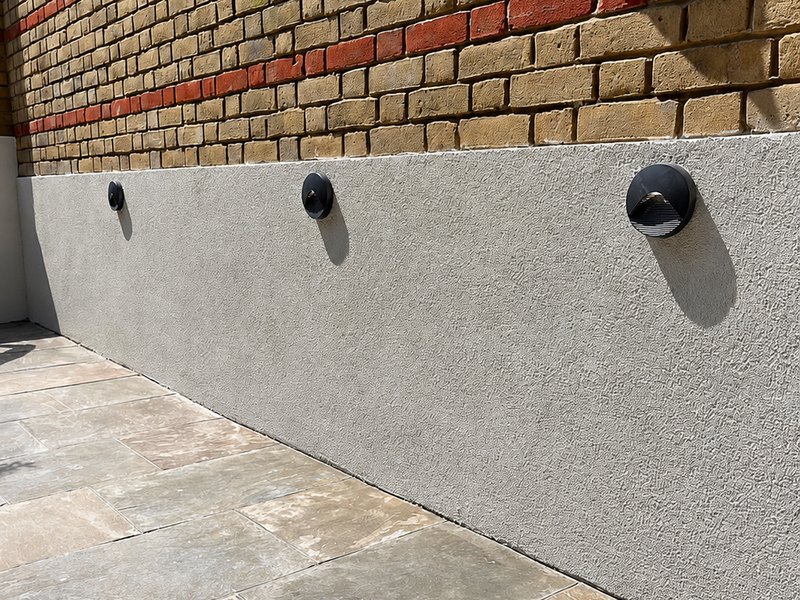 A rendered boundary wall finished in grey beside a paved patio