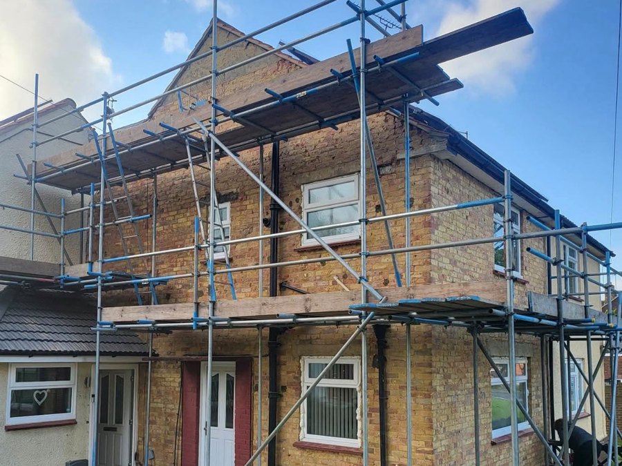 The same elevation with the old render stripped off and the yellow stock brickwork exposed, scaffolding in place