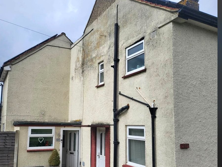 A tired elevation in Kent with old roughcast render, weathered and stained after years of patching and painting