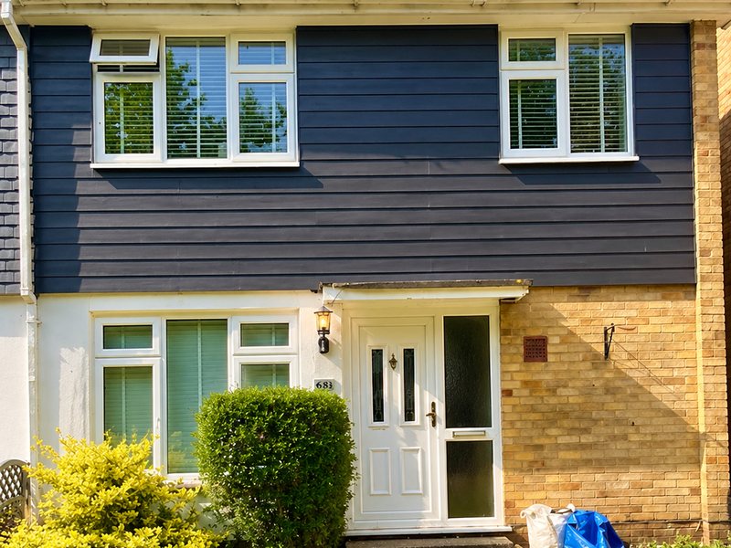 Navy cladding to the first floor of a terraced house with white render below
